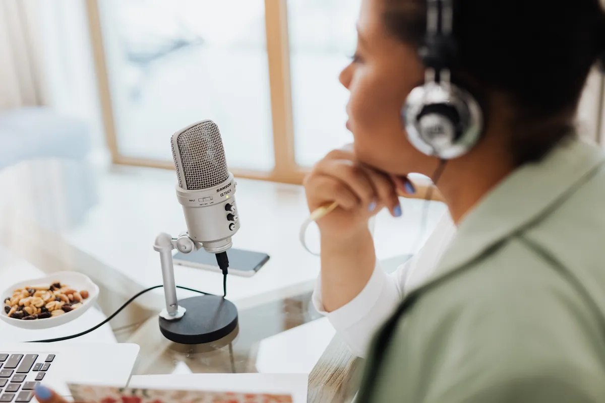 A woman in headphones listening closely beside a silver studio microphone on her desk.