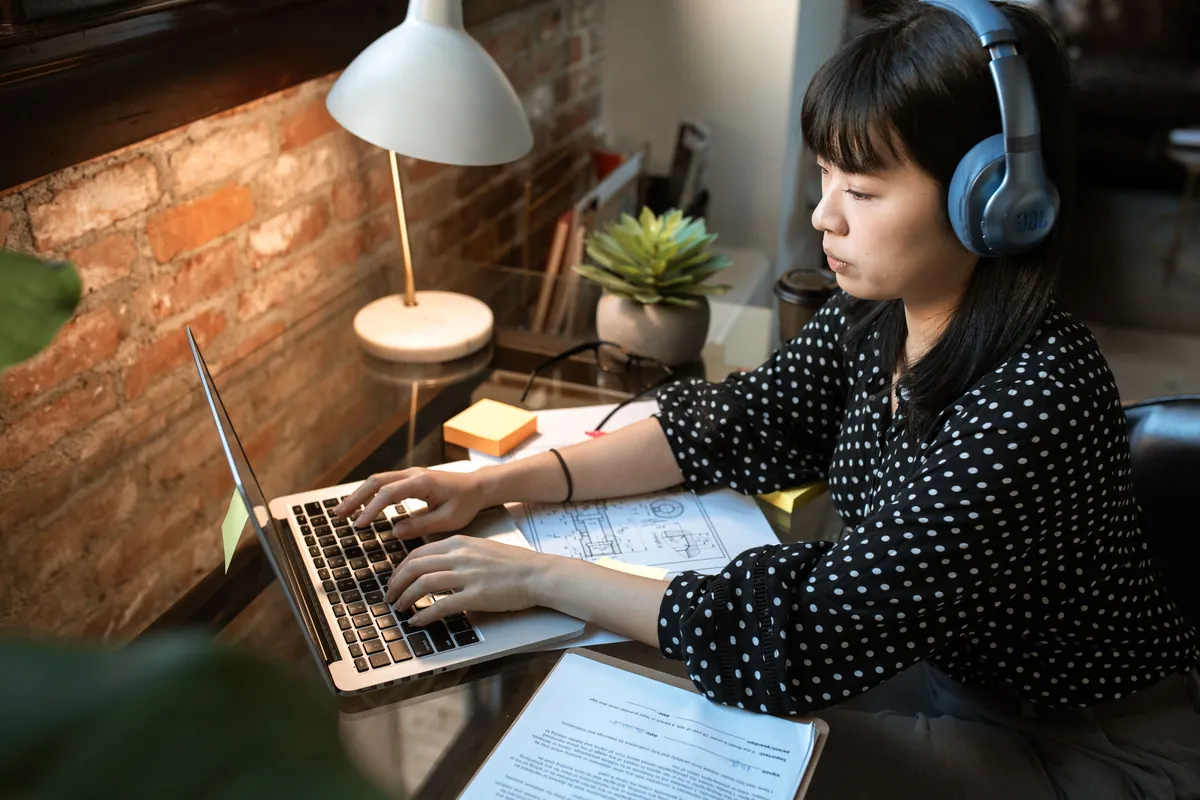 A guest in headphones at her laptop, getting ready at a desk with a warm lamp.